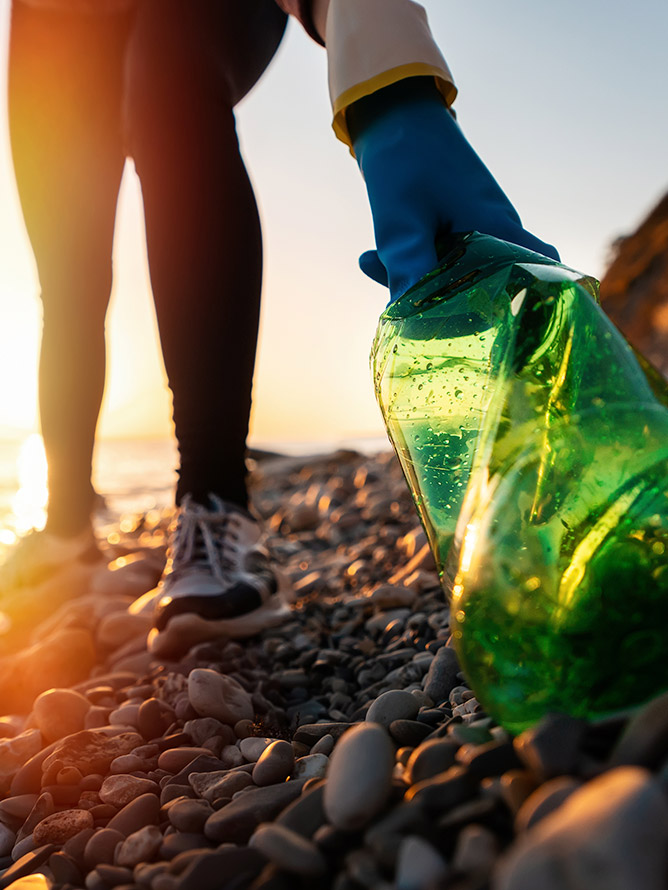 person cleaning a beach by picking up a plastic bottle